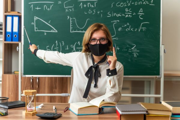 confident young female teacher wearing glasses and medical mask sits at table with school tools points at blackboard with pointer stick in classroom SSUCv3H4sIAAAAAAAACpyRwW7DIAyG75P2DhHnRiJLwtK9SrWDA6RBpVAB6TRVffcZCBXn3fBn+7d/83h/axoyg1ecfDWPGGGstN58cBCUNYjpYedOGiFdTe6uZ7QGUqhgnQJdwxkCXw1cJUKzaR3xMyWJDxA2L32cviMOQZ5RI8OXRF7xlOOmJFISOzBFyKFifpsTKyiL/6szP76LGzhLw3/TwpURJ7WEbOSUS8nlJ0h3ra3BJpStXN0tBx0L+krp5hRX5ly12bCms5c2bjcTXFzhtTnR1t5g1vHEC2rKwlfwHstF4dUgjp9sr9UcY0MysKsSgT8Rw67/GMfxeJz64XNklNFuL8i/tyrUSesUIYz5RYnauoobEMqGaWB0aGknWDt042c7iWlpe867peN0WNiIh3/+AQAA//8DANsT6FeYAgAA